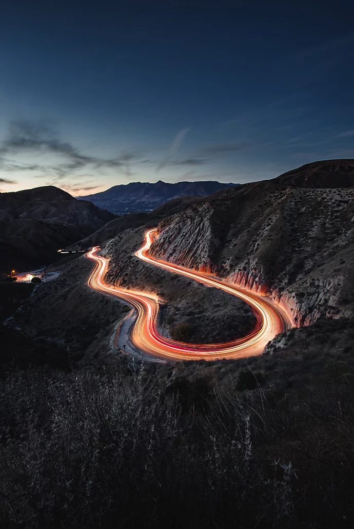 Light trails hovering over a hillside roadway from a car driving through