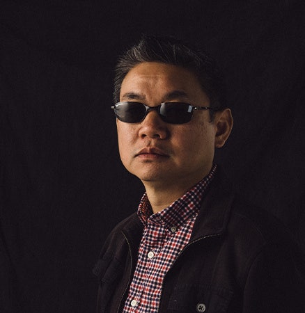 Headshot photo of a man with sunglasses wearing a blue and red checkered shirt