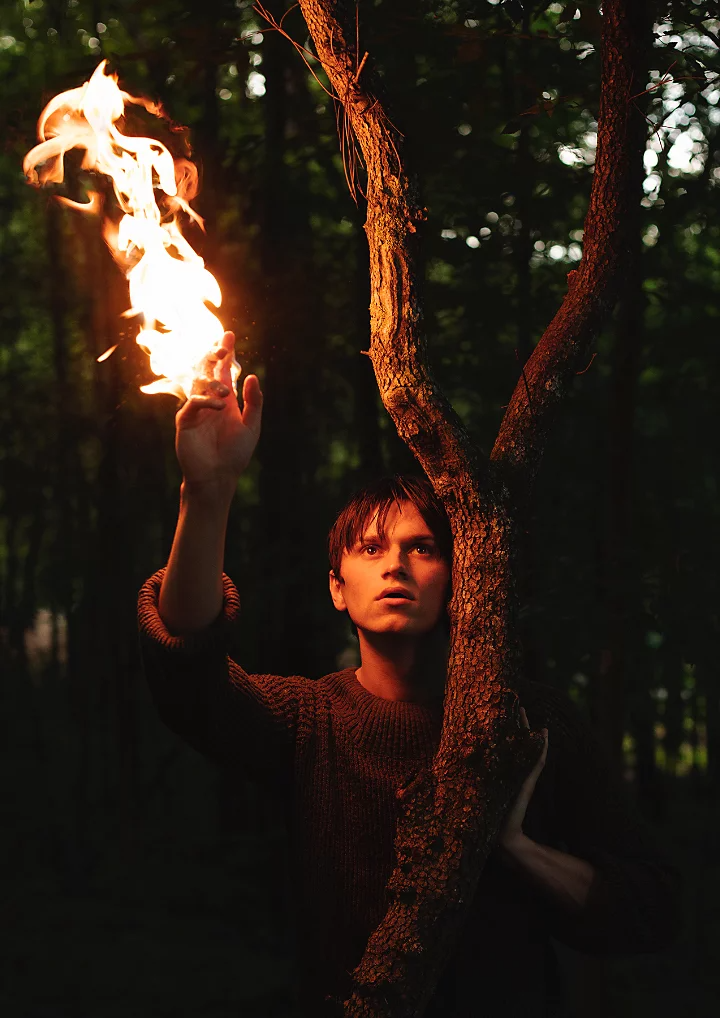 A person standing next to a tree with their hand raised up and on fire