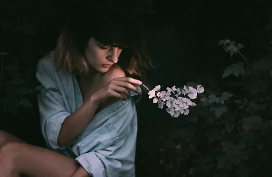 A person sitting and reaching out to touch a flower next to them