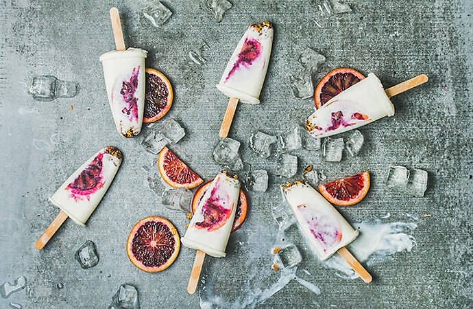 Blood orange popsicles and slices arranged on a concrete colored backdrop