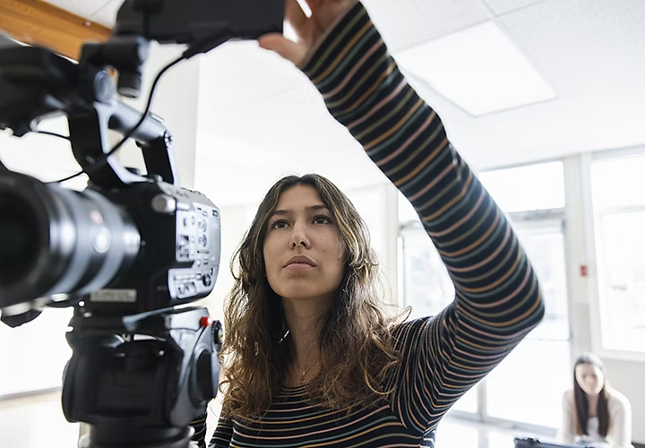 A videographer looking into the viewfinder of a camera setup on a tripod