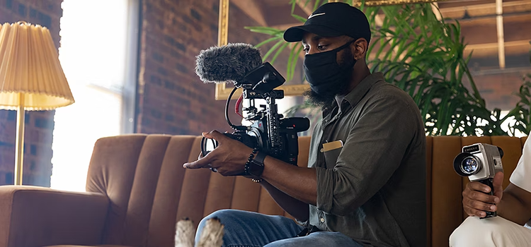 A videographer sitting on a couch prepping their camera for some videography