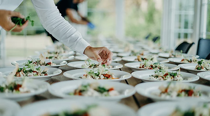 A caterer putting finishing garnishes on a large number of meals for an event