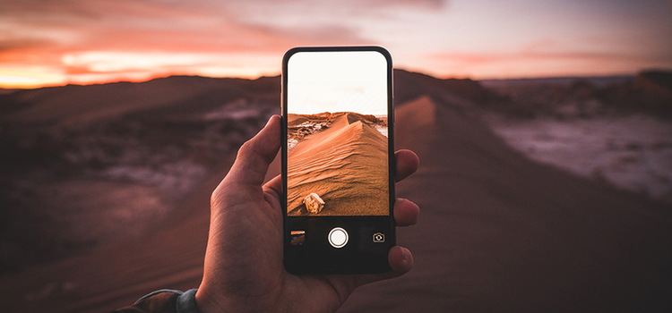 A person holding a smartphone and taking a photo of a desert environment