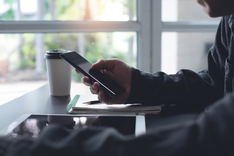 Man holding and using a smartphone device with a cup of coffee next to it.