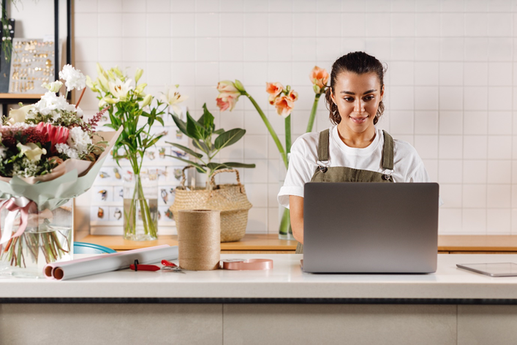 Photo of the owner of a flower shop working on a laptop at the counter.