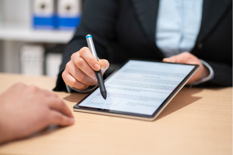 A business professional grips a tablet showcasing a digital contract, preparing to sign with a stylus, as the client's hand reaches out to take the stylus.