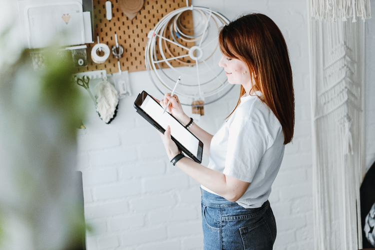 Female standing in a room with clothing design tools working on a tablet.