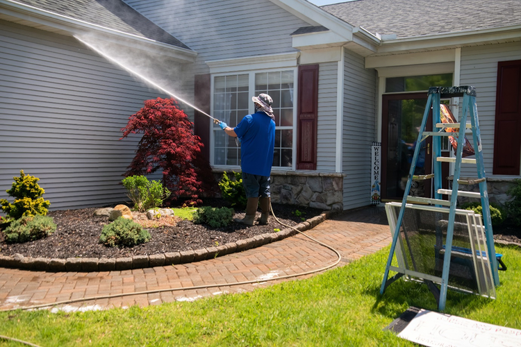 Photo of a man using a power washer to clean the windows and front of a house.