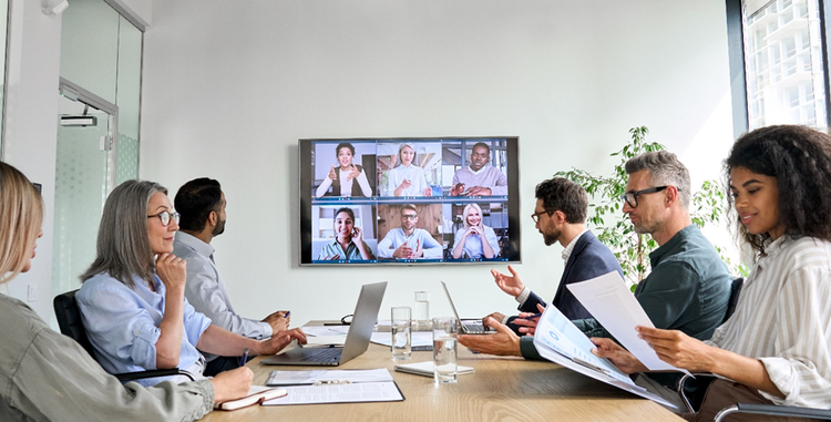 Photo of a team meeting involving people both working in the office and participating via video conferencing.