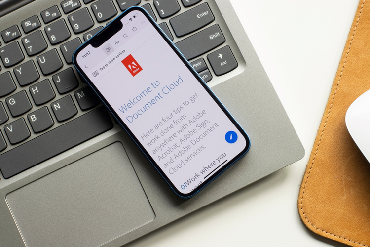 Mobile phone on top of a laptop. Displayed on the phone screen is the Adobe logo and the text "Welcome to Document Cloud" with a brief description.