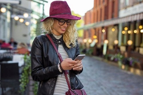 Woman smiling at iPhone on the street.