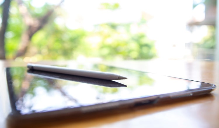 A tablet lies face-up on a table with a compatible electronic pen atop its screen.