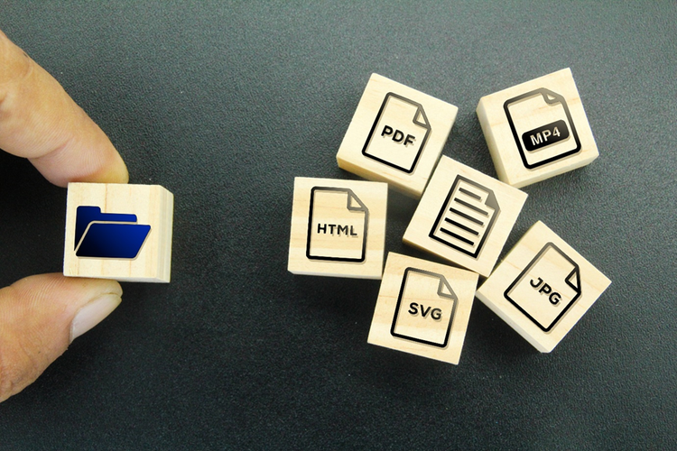 Series of wooden blocks depicting different file formats including PDF, JPG, txt, html, m4, being assembled to go into a block with a folder icon behind held by a person's hand.