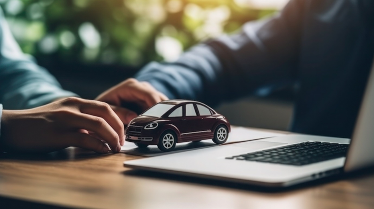 Photo of the hands and arms of two people sitting at a desk with a laptop and a model car.