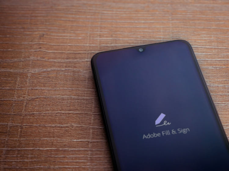 Photo of a mobile phone on a desk with Adobe Fill & Sign displayed on the screen.