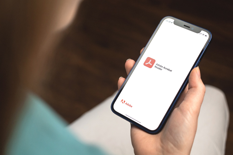 A hand holds a phone with a screen displaying the Adobe Acrobat Reader app.