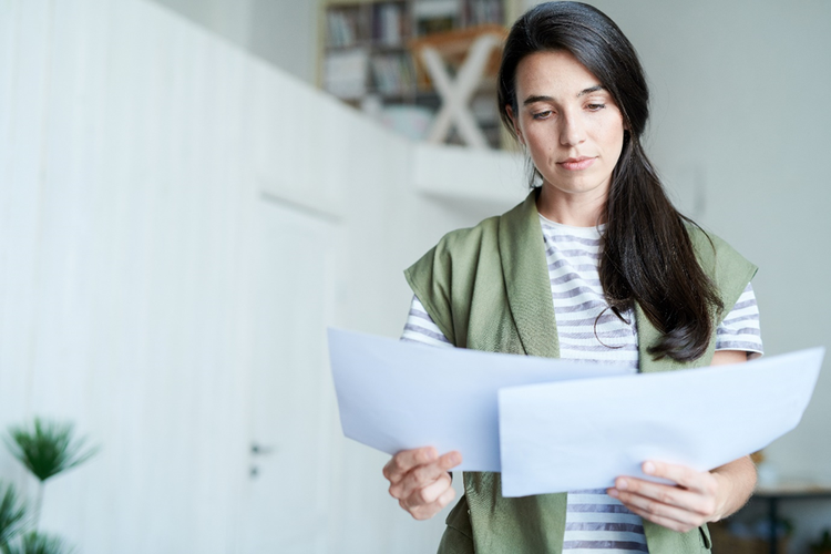 Photo of a woman holding and comparing two paper documents side-by-side.