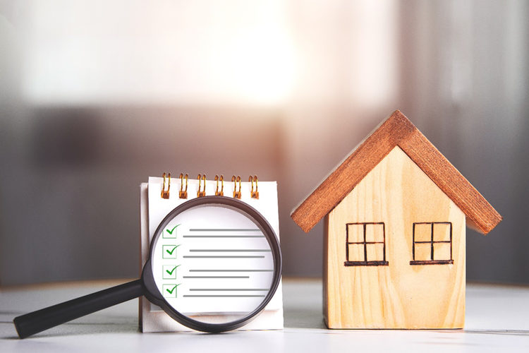 Small wooden model of a house on a table with a checklist and magnifying glass.