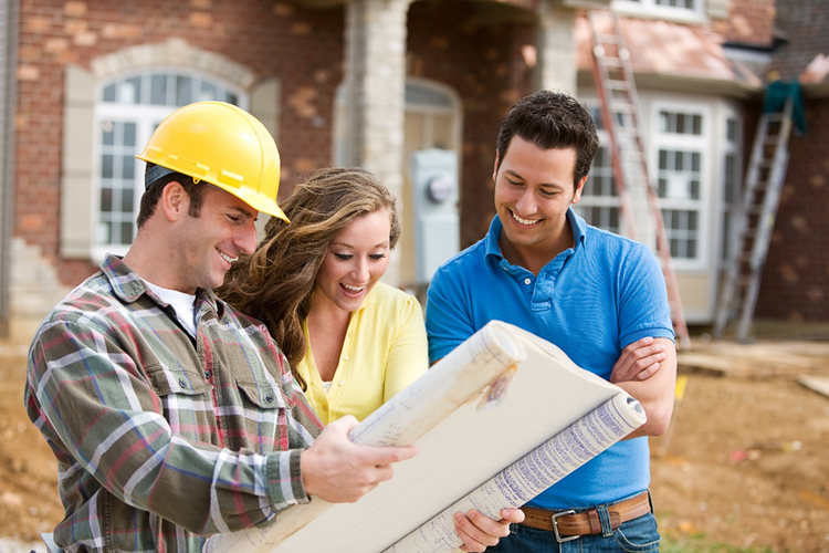 Photo of three people reviewing plans on home building site.