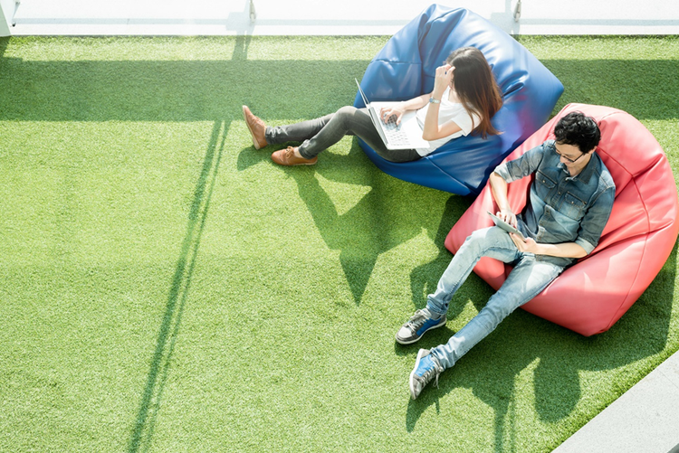 Male and female sitting on beanbags. One is reading on a laptop, the other on a tablet.