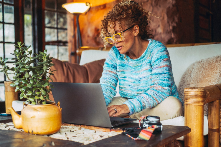 Photo of a woman sitting on a couch at home working on a laptop on a coffee table.