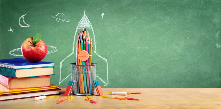 Photo of books, pencils, paperclips and an apple on a desk. A chalkboard in the background has the outline of a rocket ship around the pencil container.