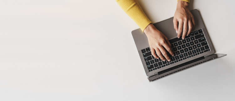 Photograph looking person's hands typing on a laptop keyboard from above.