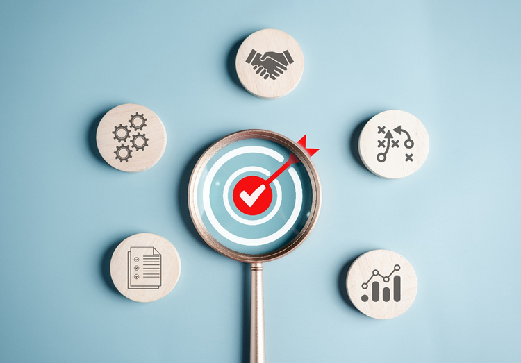 Diagram showing a central target under a magnifying glass. Surrounding it are icons on blocks depicting documentation, plans, collaboration, and processes.