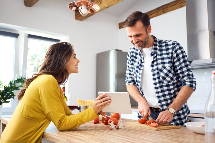 Photo of a couple cooking in the kitchen while referring to a digital tablet.