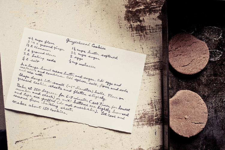 Handwritten recipe on a card for gingerbread cookies beside a tray with the dough cut into biscuit shapes.