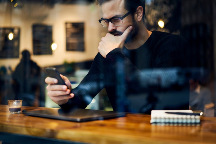 Man holding his phone with his right hand while resting his head in his left hand.