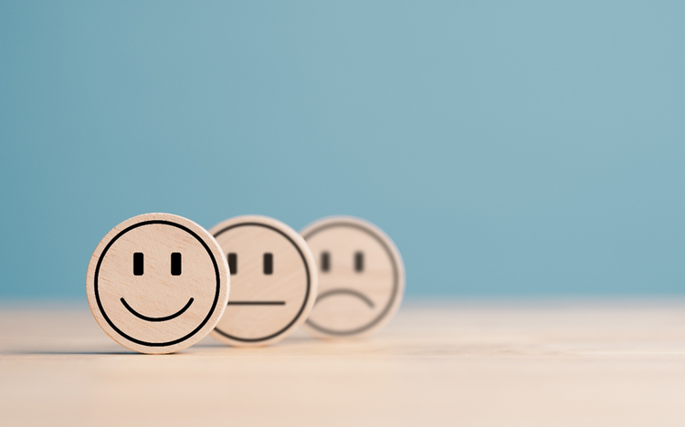Photo of three wooden blocks depicting happy, neutral and unhappy faces.