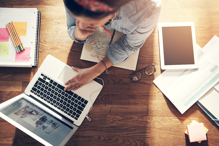 Photo of a female entrepreneur sitting at a desk with a laptop, tablet, notebooks, and post-it notes.