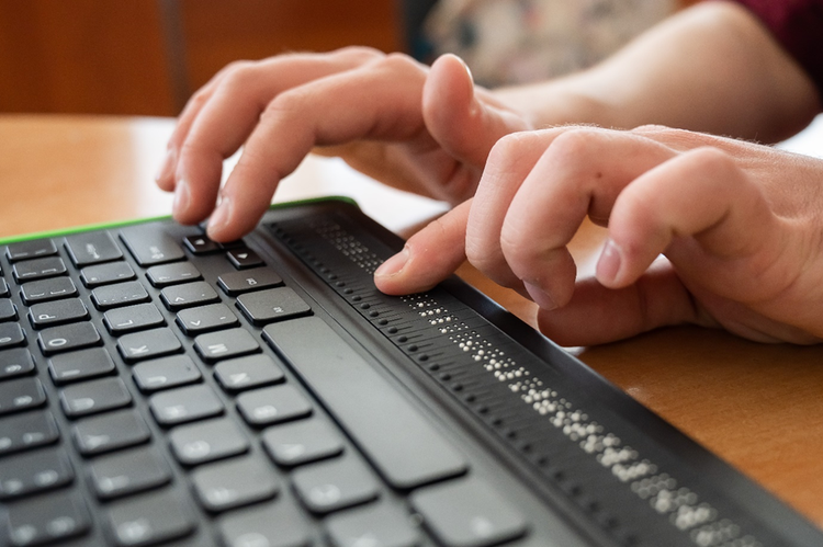 Photo of a person's hands using a keyboard with a Braille display.