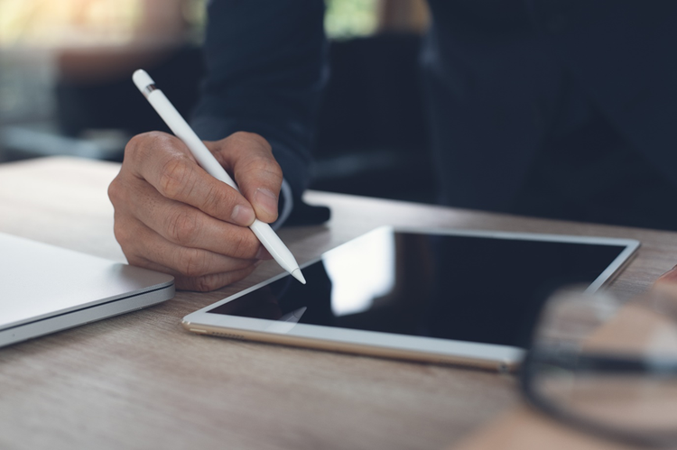 A hand holds a digital pen above the screen of a tablet.