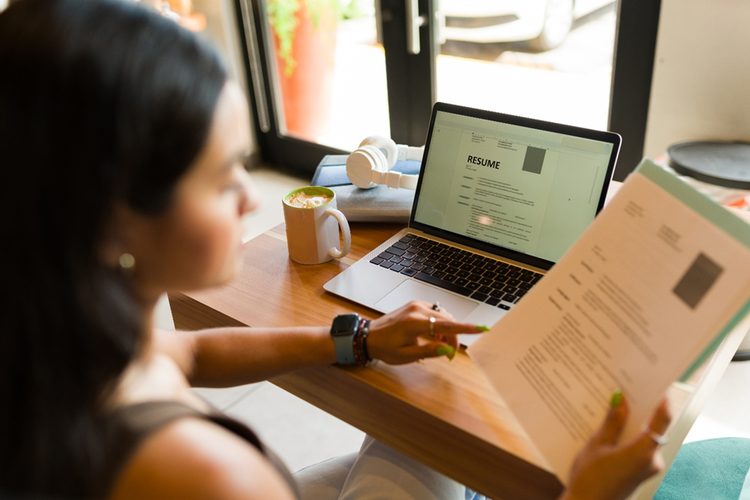 Photo of a female sitting at a table with a laptop working on a resume.