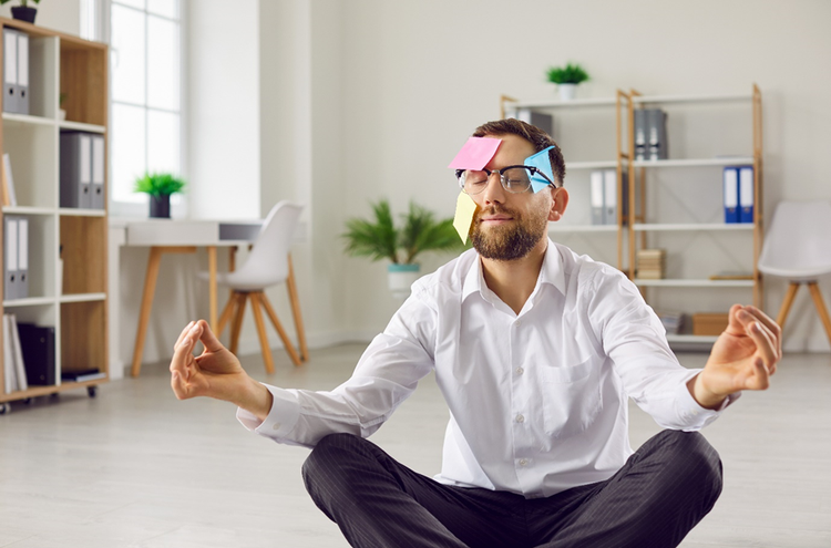 Humorous photo of a man sitting on the floor in a meditative pose with sticky notes on his face.