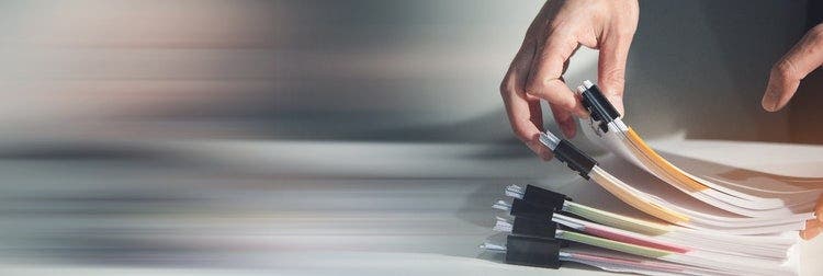 Paper documents held together with clips and pages flagged with coloured sticky notes.