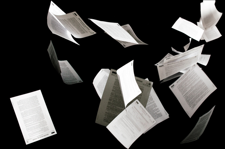 Photo of paper documents flying in the air. The pages have a combination of text and forms and all are headed with an image of a company logo.