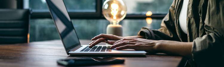 Casually dressed person sitting working on a laptop with a lightbulb in the background.