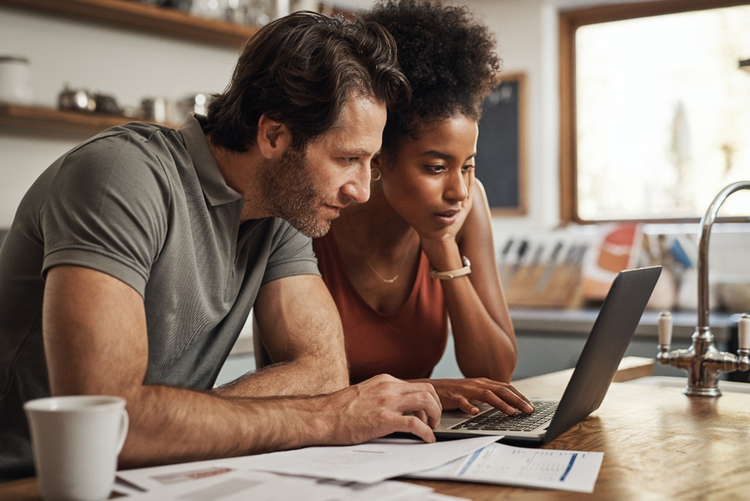 Photo of a couple sitting at a kitchen bench at home with a laptop and paperwork.