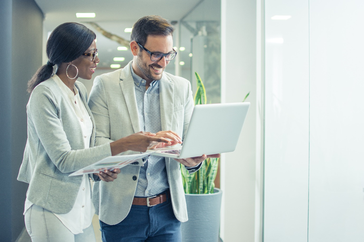 Photo of two people smiling and looking at a laptop screen in office.