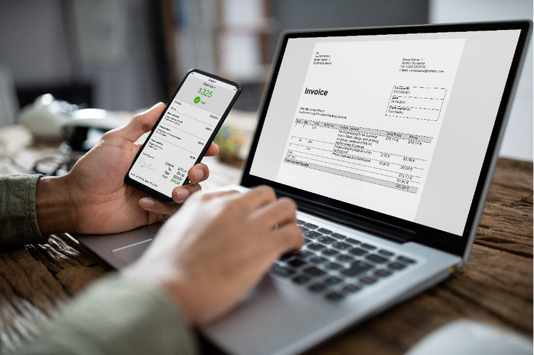 A person holds phone displaying account info next to laptop screen showing corresponding invoice.