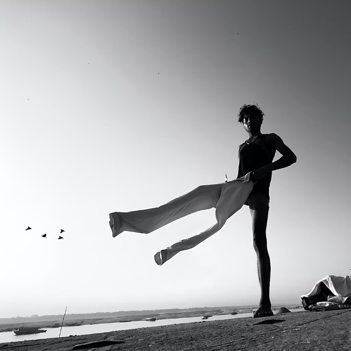 Black-and-white photo of a person putting on pants at the beach