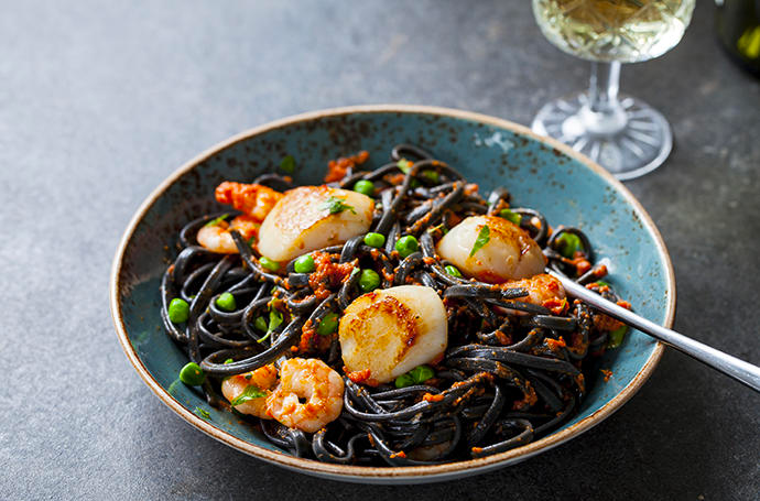 Lovely food image of squids ink pasta with seafood and a glass of white wine