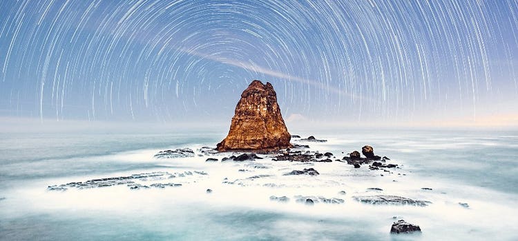 View of ocean with star trails behind it