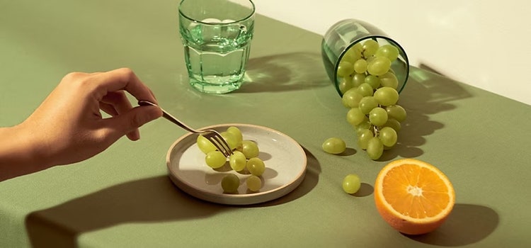 Grapes, a cut orange and glass of water on a tabletop.