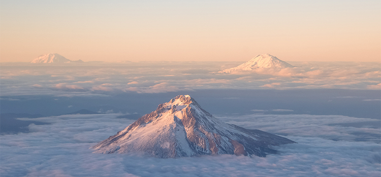 An aerial view of mountains cutting through clouds into clear sky